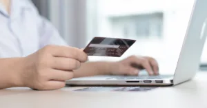 Pessoa usando cartão de crédito em compra online no notebook, representando situação de cobrança indevida