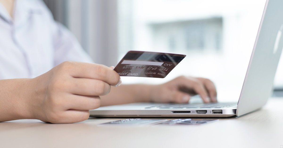 Pessoa usando cartão de crédito em compra online no notebook, representando situação de cobrança indevida
