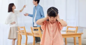 Criança tapando os ouvidos enquanto os pais discutem, representando os efeitos da alienação parental