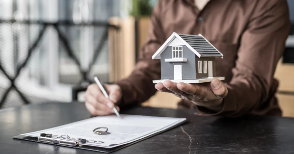 Pessoa segurando maquete de casa enquanto assina contrato de compra e venda de imóvel