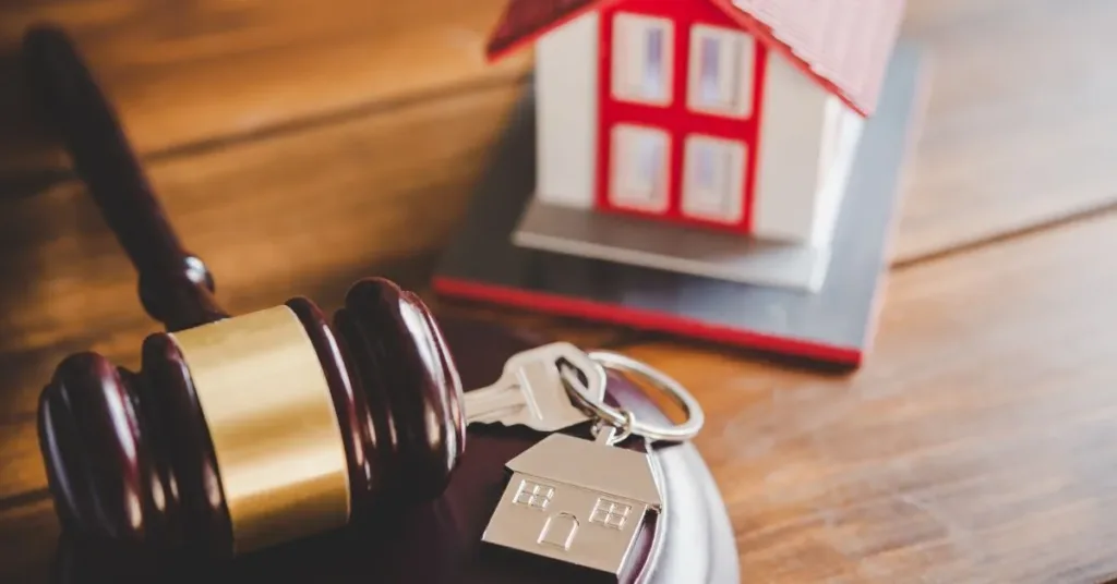 Chave de imóvel com pingente de casa ao lado de martelo da justiça e maquete de residência