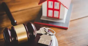 Chave de imóvel com pingente de casa ao lado de martelo da justiça e maquete de residência