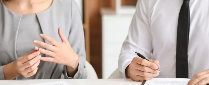 Mulher retirando aliança ao lado de advogado com documentos de divórcio consensual