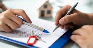 Assinatura de contrato de compra e venda de imóvel com chave e maquete de casa ao fundo