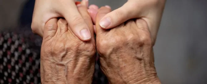Mãos de uma pessoa jovem segurando as mãos de um idoso, representando apoio e cuidado na curatela judicial