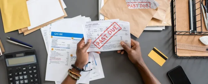 Pessoa segurando boletos vencidos sobre mesa com contas e calculadora – ilustra atraso no aluguel