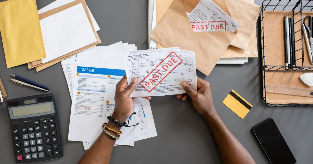 Pessoa segurando boletos vencidos sobre mesa com contas e calculadora – ilustra atraso no aluguel