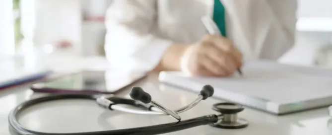 Estetoscópio sobre mesa médica com profissional ao fundo preenchendo prontuário psiquiátrico