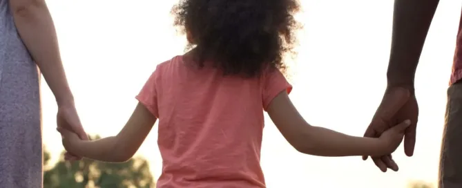 Criança de mãos dadas com dois adultos representando uma família adotiva no Brasil.