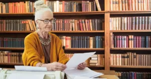 Idosa analisando documentos em biblioteca jurídica, representando decisão sobre alteração de testamento.