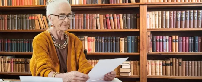 Idosa analisando documentos em biblioteca jurídica, representando decisão sobre alteração de testamento.