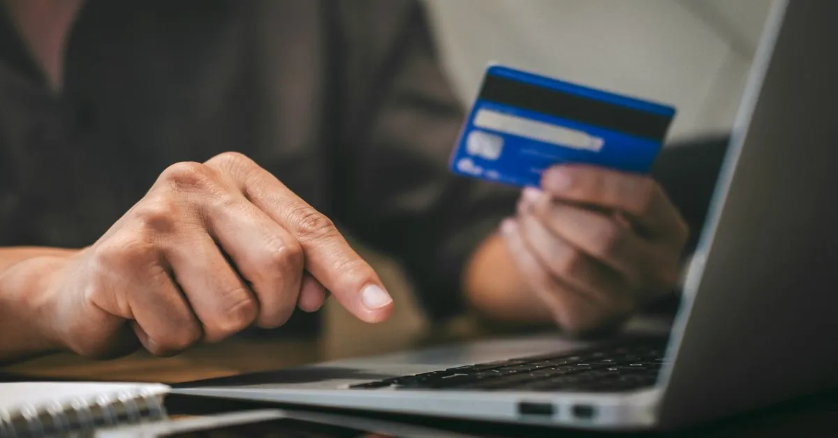 Pessoa segurando cartão de crédito e digitando no notebook para cancelar compra online