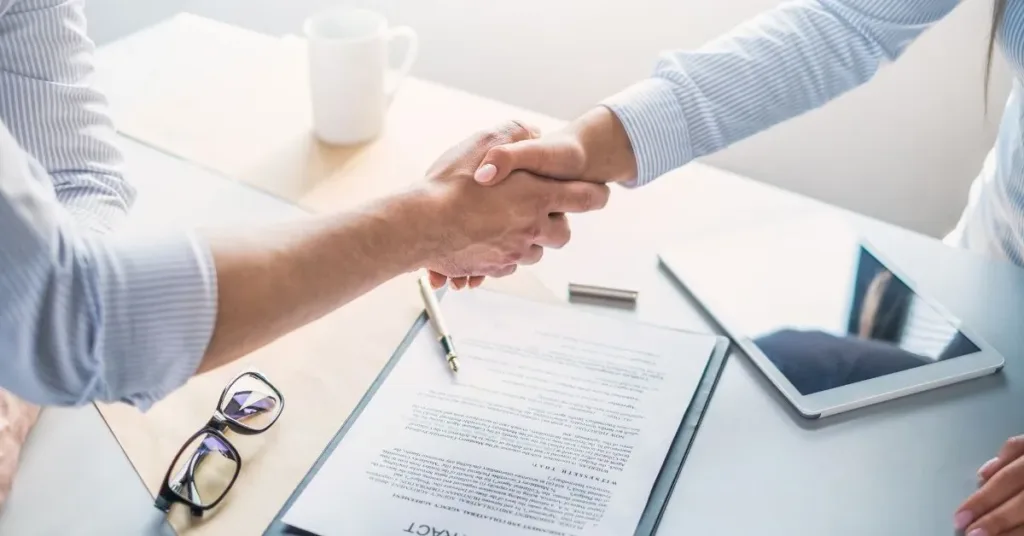 Duas pessoas apertando as mãos sobre contrato de prestação de serviços assinado