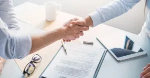 Duas pessoas apertando as mãos sobre contrato de prestação de serviços assinado