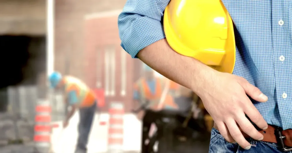 Homem segurando capacete de obra em frente a trabalhadores em construção no condomínio