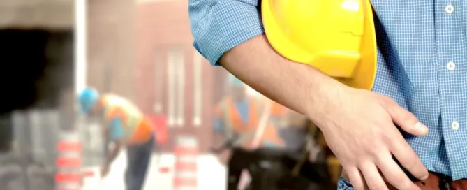 Homem segurando capacete de obra em frente a trabalhadores em construção no condomínio