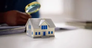 Casa em miniatura sob análise com lupa, representando venda de imóvel em inventário