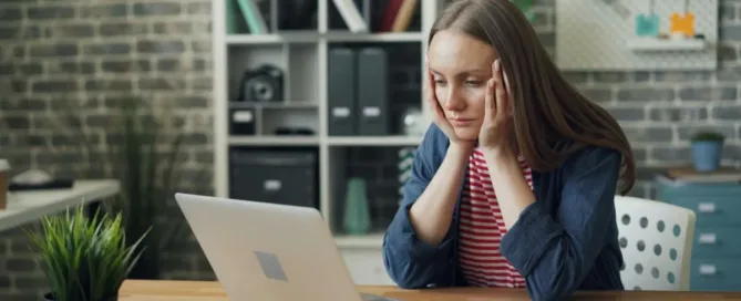 Mulher preocupada usando o computador, representando vítima de fraude com dados pessoais.