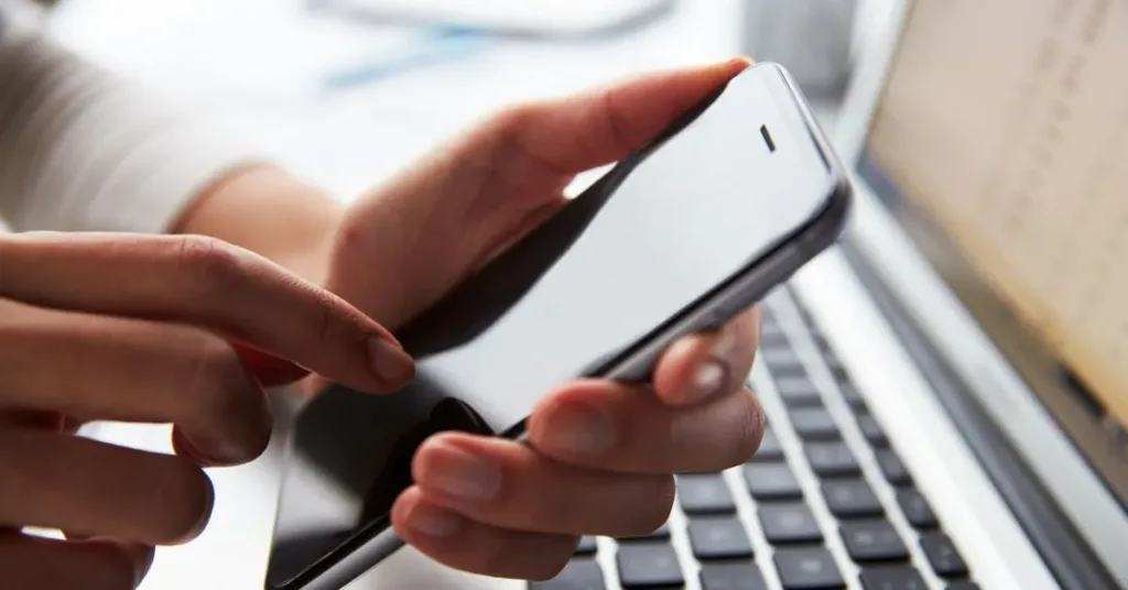 Pessoa segurando celular próximo ao notebook, simbolizando gravação de conversa como prova judicial.
