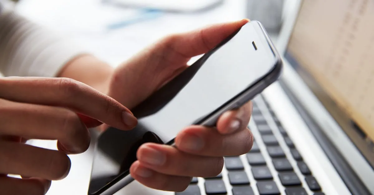 Pessoa segurando celular próximo ao notebook, simbolizando gravação de conversa como prova judicial.