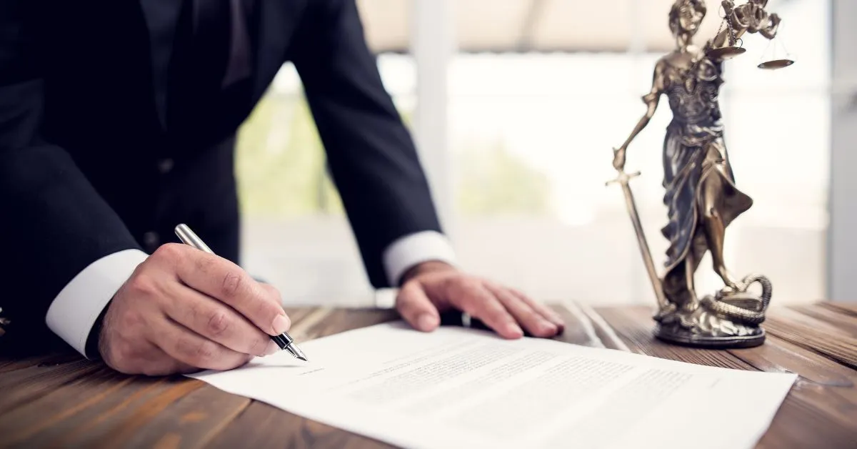 homem assinando documento jurídico ao lado de estátua da justiça, representando testamento particular ou público