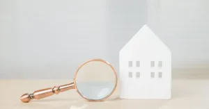 Casa em miniatura com lupa representando análise de contrato de compra e venda de imóvel que pode ser anulado