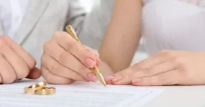 casal assinando documento com alianças sobre a mesa representando pacto antenupcial e proteção patrimonial no casamento