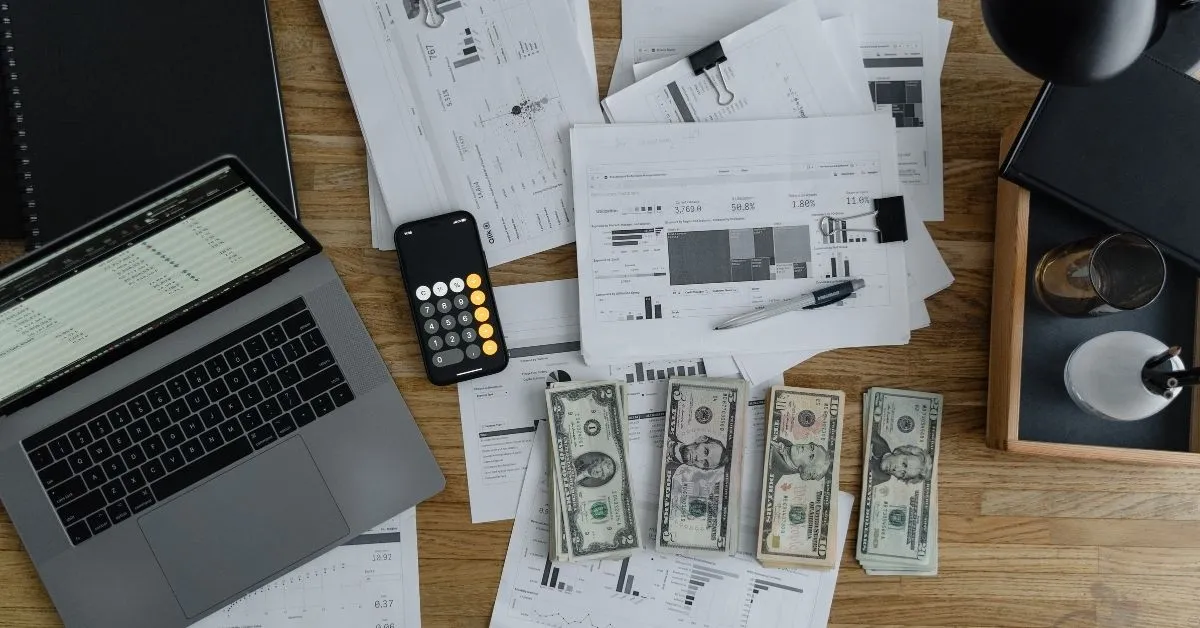 Documentos financeiros, notebook, calculadora e dinheiro sobre mesa de trabalho