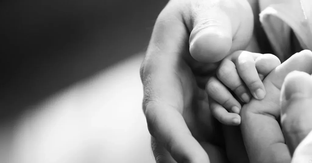 Mão de bebê apoiada na mão de um adulto, simbolizando reprodução assistida e filiação.