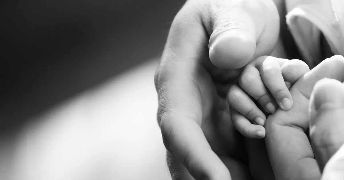 Mão de bebê apoiada na mão de um adulto, simbolizando reprodução assistida e filiação.