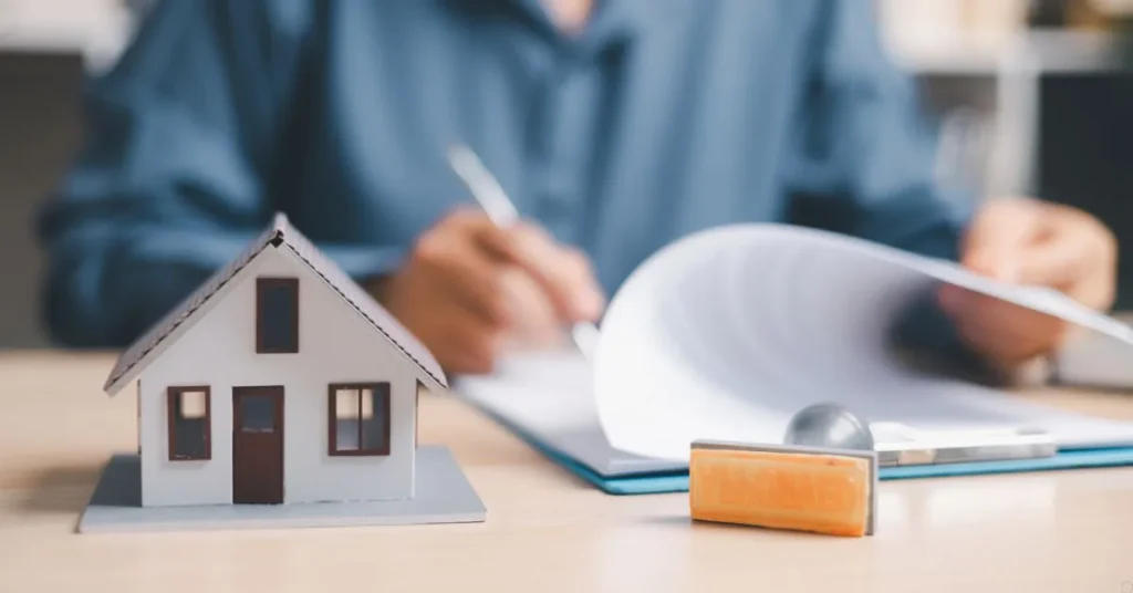 Miniatura de casa ao lado de contrato sendo assinado e carimbo, representando contrato de gaveta de imóvel e seus riscos jurídicos.