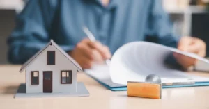 Miniatura de casa ao lado de contrato sendo assinado e carimbo, representando contrato de gaveta de imóvel e seus riscos jurídicos.