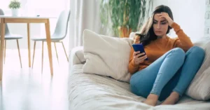 Mulher preocupada olhando o celular após identificar possível fraude em conta digital.