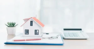Miniatura de casa, chaves e calculadora sobre documentos, representando imóvel com dívida de IPTU ou condomínio após a compra.