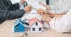 Casas em miniatura e chaves sobre mesa durante reunião, representando imóvel com inventário em andamento e negociação entre herdeiros.