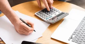 Pessoa realizando cálculos com calculadora e documentos sobre pensão alimentícia, horas extras, PLR e bônus.