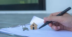 Casa em miniatura, chaves e documentos representando imóvel em nome de pessoa falecida e sua regularização.