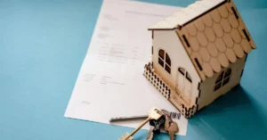 Casa em miniatura, chaves e documentos representando inventário de imóvel e transferência da propriedade aos herdeiros.